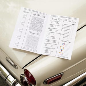 Pode incluir: Um livreto de atividades de casamento branco com texto e gr&aacute;ficos pretos. As se&ccedil;&otilde;es incluem jogo da velha, um labirinto intitulado Love Finds a Way, um ca&ccedil;a-palavras chamado Marriage Vows, um quiz de casamento, The Shoe Game e um jogo de adivinha&ccedil;&atilde;o Emoji Songs.
