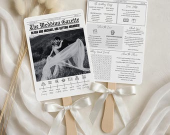 May include: Two wedding fans with wooden handles and white ribbon bows. The fans are printed with a newspaper-style design. One fan features a black and white photo of a couple, the text "The Wedding Gazette," and a wedding timeline. The other fan includes wedding party details and a word search.