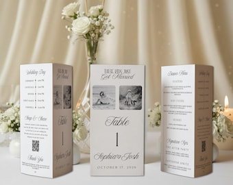 May include: Three white rectangular wedding table cards with black text. The center card displays 'These Kids Just Got Married', two black and white photos, 'Table 1', 'Sophia & Josh', and 'October 17, 2026'. The side cards show a wedding day timeline, menu, and QR code.