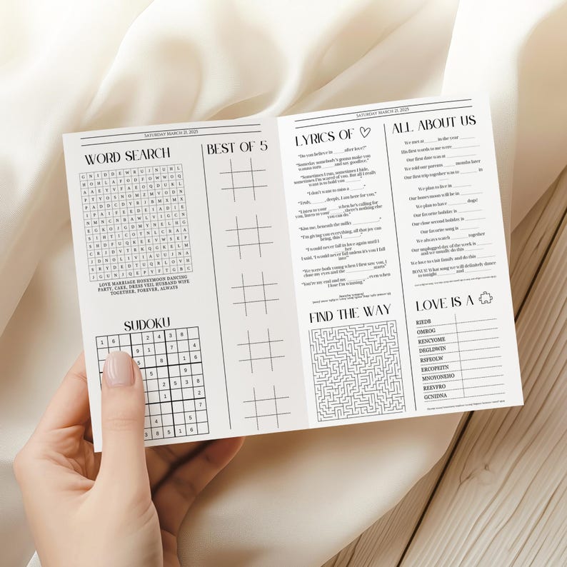 May include: A white paper activity booklet featuring black text and graphics. Sections include a word search, Sudoku, tic-tac-toe, a lyrics quiz, an 'All About Us' questionnaire, a maze, and a word scramble game titled 'Love Is A'.