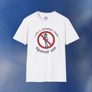 以下が含まれることがあります： 「I am a Christian mom against vox」の文字が黒と赤でプリントされた白いTシャツ。デザインには、漫画のキャラクターに線が引かれた赤い円が含まれています。このシャツは半袖で、クルーネックです。