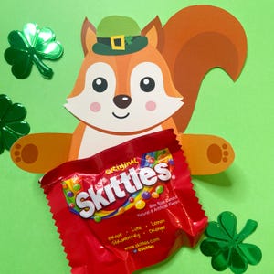 May include: A red and white Skittles candy bag with the text "Original Skittles" and a green shamrock on top. The bag is held by a cartoon squirrel wearing a green leprechaun hat.