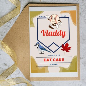 May include: A greeting card with a baseball theme. The card features a cartoon baseball character, a blue jay, and a red maple leaf. Text on the card reads "Who's your Vladdy? Swing Big Eat Cake Be Legendary."