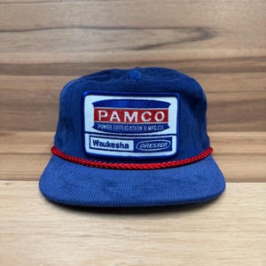 May include: A blue corduroy baseball cap with a red rope trim. The cap features a large embroidered patch with the text "PAMCO POWER APPLICATION & MFG. CO. Waukesha DRESSER".