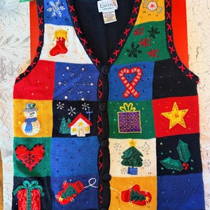 May include: A sleeveless button-down knit vest featuring a colorful patchwork design with various holiday-themed embroidered motifs including a snowman, candy canes, presents, a house, and snowflakes, accented with sequins on a black background.