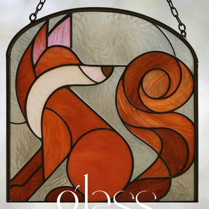 May include: Stained glass panel featuring a stylized fox in shades of orange, brown, and white. The fox is set against a light gray background within a black metal frame. The words "glass sanctuary" are written in white script.