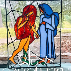 Puede incluir: Panel de vidrieras con dos figuras en colores vibrantes. Una figura tiene cabello rojo y ropa naranja, la otra es azul. El panel está enmarcado en negro con las palabras "Glass Sanctuary" en la parte inferior.