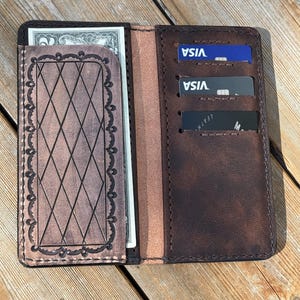 May include: Open brown leather wallet with multiple card slots and a cash pocket. The wallet features a decorative diamond pattern and a border design on the cash pocket. Several credit cards are visible in the card slots, and a banknote is in the cash pocket.