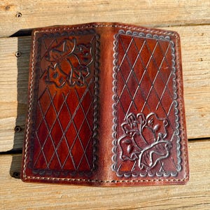Puede incluir: Cartera de cuero marrón abierta, con patrones florales y de diamantes en relieve. La cartera está hecha de cuero marrón oscuro y rico, con intrincados repujados. El interior es visible, mostrando el diseño y la artesanía de la cartera.