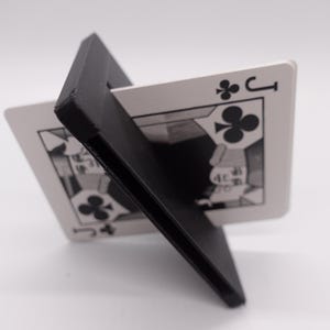 May include: A black plastic card holder with a playing card, the Jack of Clubs, inserted into it. The card is held at an angle, so the face of the card is visible.