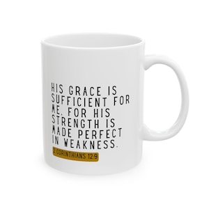 May include: A white ceramic mug featuring black sans-serif text that reads: HIS GRACE IS SUFFICIENT FOR ME, FOR HIS STRENGTH IS MADE PERFECT IN WEAKNESS. Below the text is a gold-colored rectangular accent with the words 2 CORINTHIANS 12:9.