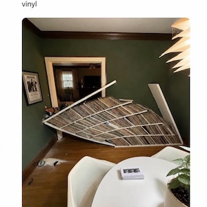 K&ouml;nnte beinhalten: Ein eingest&uuml;rztes wei&szlig;es Regal voller zahlreicher Schallplatten, das in einem spitzen Winkel an einer dunkelgr&uuml;nen Wand lehnt. Der Text oben lautet: Note to self don't ever use furniture from IKEA for vinyl. Das Regal ist zerbrochen und schief.