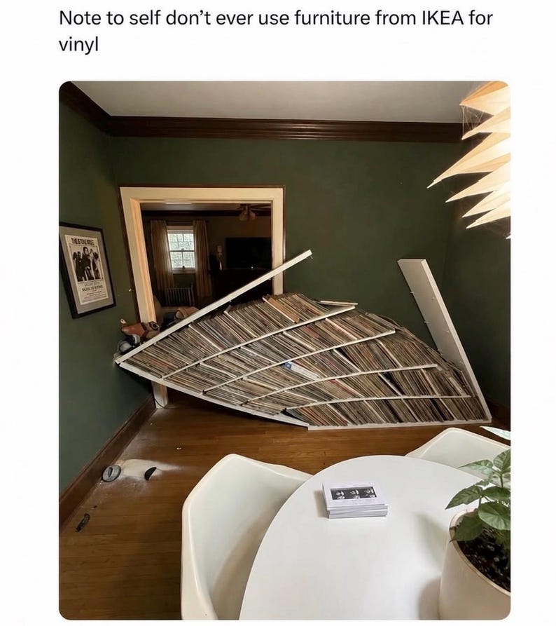 K&ouml;nnte beinhalten: Ein eingest&uuml;rztes wei&szlig;es Regal voller zahlreicher Schallplatten, das in einem spitzen Winkel an einer dunkelgr&uuml;nen Wand lehnt. Der Text oben lautet: Note to self don't ever use furniture from IKEA for vinyl. Das Regal ist zerbrochen und schief.