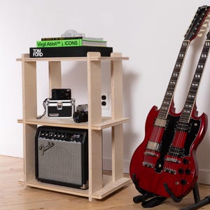 K&ouml;nnte beinhalten: Ein dreist&ouml;ckiges Regal aus hellem Sperrholz mit B&uuml;chern mit den Titeln Virgil Abloh ICONS und Tom Ford, einer schwarzen Kamera und einem Fender-Verst&auml;rker. Neben dem Regal steht eine kirschrote Doppelhals-E-Gitarre auf einem schwarzen St&auml;nder.