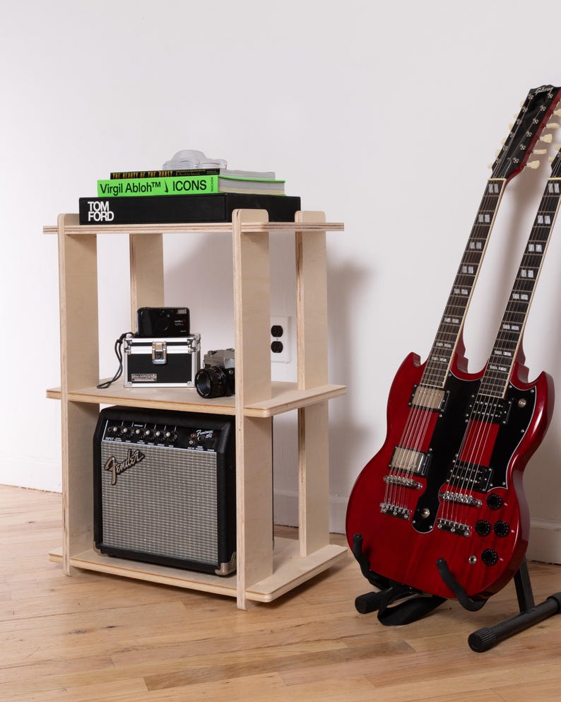 K&ouml;nnte beinhalten: Ein dreist&ouml;ckiges Regal aus hellem Sperrholz mit B&uuml;chern mit den Titeln Virgil Abloh ICONS und Tom Ford, einer schwarzen Kamera und einem Fender-Verst&auml;rker. Neben dem Regal steht eine kirschrote Doppelhals-E-Gitarre auf einem schwarzen St&auml;nder.