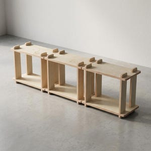 K&ouml;nnte beinhalten: Ein modulares Regal aus hellem Holz mit drei miteinander verbundenen quadratischen F&auml;chern. Das Design verwendet eine Steckverbindung mit sichtbaren Verbindungsstellen an den Ecken, wodurch eine niedrige Aufbewahrungsstruktur entsteht.