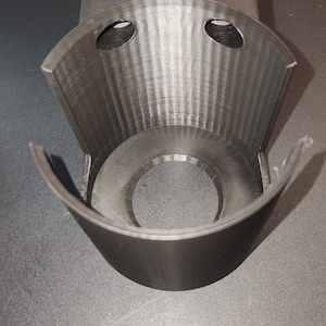 Puede incluir: Un portavasos de plástico negro impreso en 3D con dos agujeros en la parte superior y un diseño curvo.