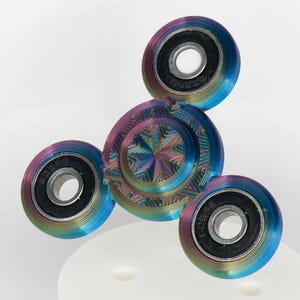 May include: A rainbow colored metal fidget spinner with three spinning sections. The center section has a starburst pattern.