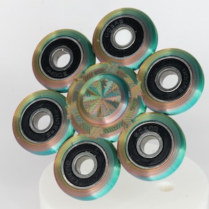 May include: A multi-colored fidget spinner with six round, spinning sections. Each section has a silver bearing in the center and the word "SCORES" printed on the outer edge.