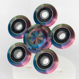 May include: A rainbow colored fidget spinner with five metal bearings. The spinner has a star-shaped design in the center.