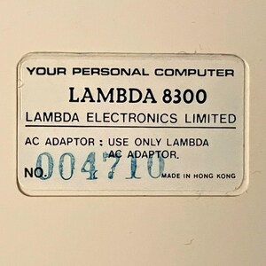 May include: A white label with black text that reads "YOUR PERSONAL COMPUTER LAMBDA 8300 LAMBDA ELECTRONICS LIMITED AC ADAPTOR: USE ONLY LAMBDA AC ADAPTOR. NO. 004710 MADE IN HONG KONG".