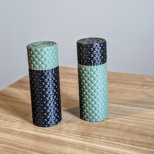 May include: Two cylindrical objects with a black and green honeycomb pattern. The objects are made of a textured material and are approximately 7.5 cm tall.