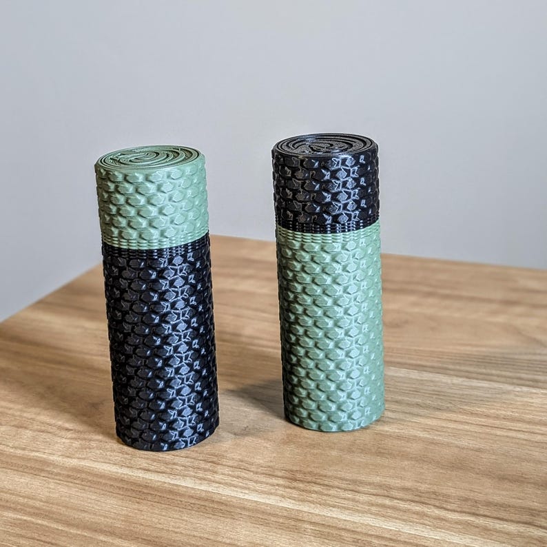 May include: Two cylindrical objects with a black and green honeycomb pattern. The objects are made of a textured material and are approximately 7.5 cm tall.