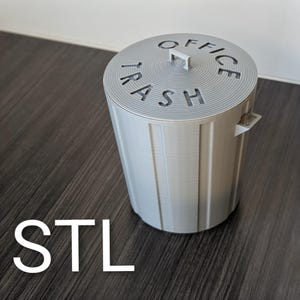 May include: A light gray office trash can with the word "TRASH" and "OFFICE" cut out on the lid. The can has a handle on the lid and two small handles on the sides. The word "STL" is at the bottom.