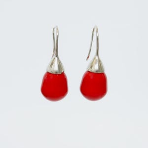 May include: A pair of red teardrop earrings with silver-coloured metal caps and ear wires. The earrings have a smooth, glossy finish and a vibrant colour. These earrings are a stylish accessory.