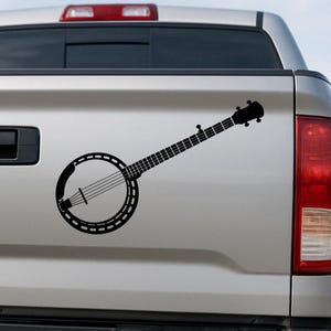 May include: Black and white silhouette of a banjo on a silver truck tailgate.