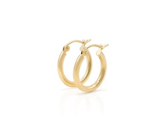 May include: A pair of gold hoop earrings. The earrings are round with a polished finish. The hoops are a medium size and have a simple, classic design. The earrings are displayed on a white background.