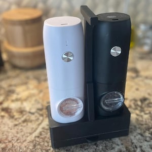 May include: A white and black electric salt and pepper grinder set with a black stand. The grinders have clear containers with visible salt and pepper.