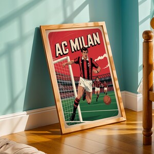 May include: A framed vintage-style poster featuring a soccer player in a black and red striped jersey, with the text "AC MILAN" at the top. The poster is set against a red background with a green field and a stadium in the distance.