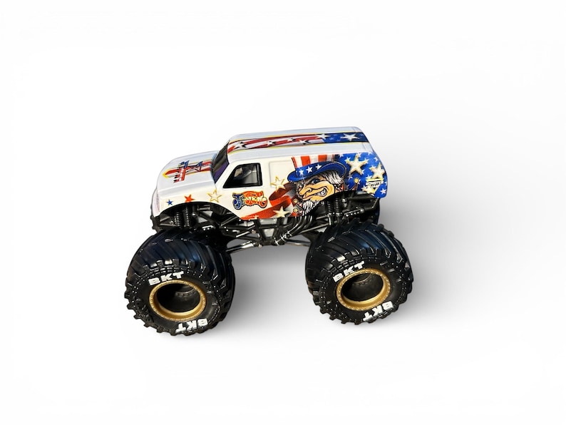 May include: A white monster truck toy with patriotic graphics, including stars, stripes, and an Uncle Sam character. The truck has large black tires with gold rims and the text "BKT". The truck's design incorporates red, white, and blue colors.
