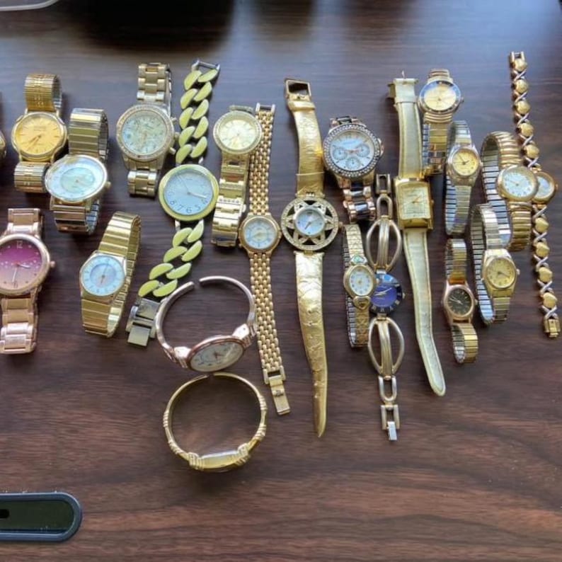 May include: A collection of gold-toned watches with various band styles, including link, chain, and bangle designs. The watch faces display different colors and designs, creating a diverse assortment of timepieces.