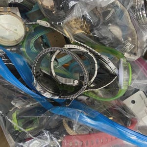 Op de afbeelding: Een verzameling verschillende polshorloges, met zilveren en gouden tinten, en verschillende bandstijlen. Sommige horloges zijn zichtbaar doorzichtige plastic zakken, met een verscheidenheid aan ontwerpen en wijzerplaten.
