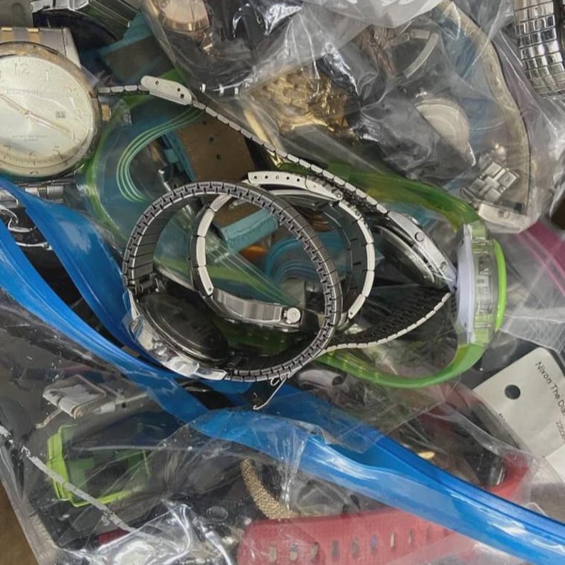 Op de afbeelding: Een verzameling verschillende polshorloges, met zilveren en gouden tinten, en verschillende bandstijlen. Sommige horloges zijn zichtbaar doorzichtige plastic zakken, met een verscheidenheid aan ontwerpen en wijzerplaten.