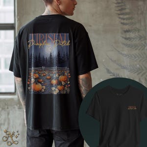 May include: Black t-shirt featuring a pumpkin patch design on the back with the text "TIRISTAL Pumpkin Patch" in gold lettering. The design includes pumpkins, a fence, and a moonlit forest scene. A smaller logo is on the front.