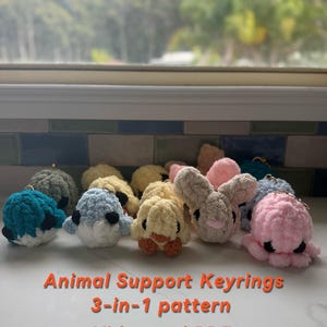 Puede incluir: Llaveros de animales de ganchillo hechos a mano en varios colores, incluyendo azul, rosa y beige. Los llaveros presentan diseños de ballena, pingüino, pato, conejo y pulpo. El texto en la imagen dice: "Animal Support Keyrings 3-in-1 pattern Video and PDF Beginner+".