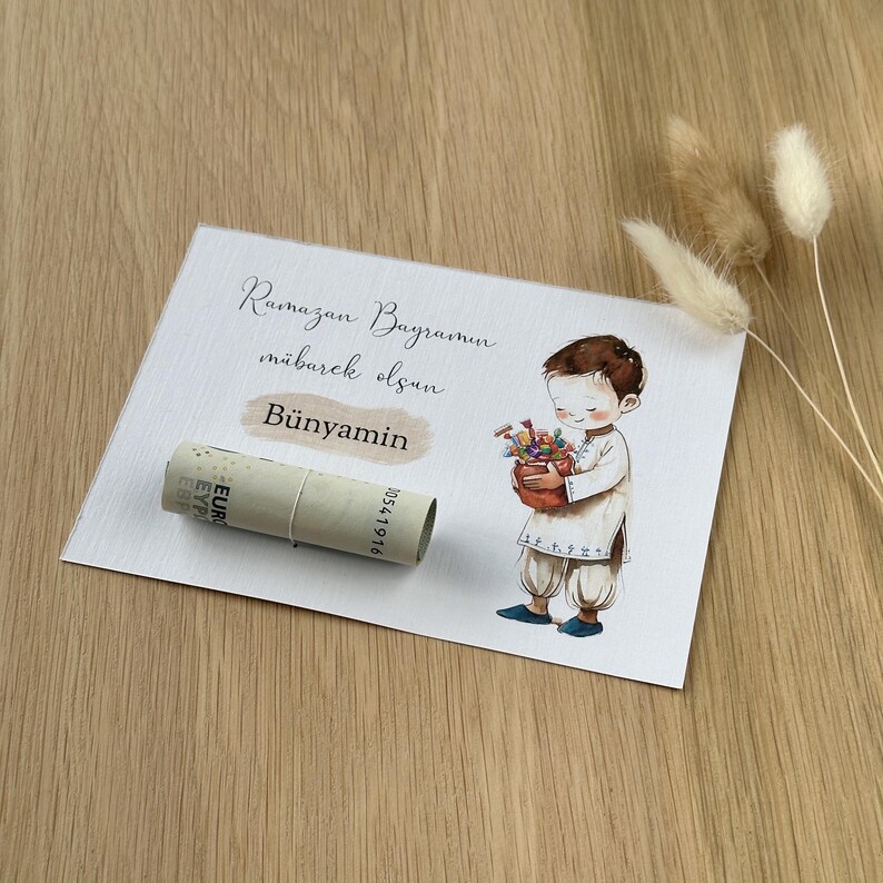 May include: A white card with the text "Ramazan Bayramin mubarek olsun" and the name "Bunyamin" written in cursive. A cartoon illustration of a boy holding a basket of flowers is on the right side of the card. A rolled-up euro bill is on the left side of the card.
