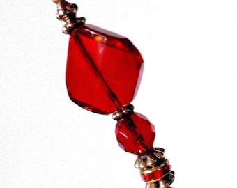 May include: A red glass pin with gold accents. The pin has a large, faceted, red glass bead at the top, followed by a smaller, faceted, red glass bead, and a gold bead. The pin is finished with a gold cap and a thin, gold wire.