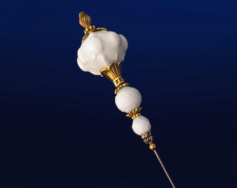May include: A white glass pin with gold accents. The pin has a large, round, white glass head with a smaller, round, white glass bead below it. The pin is on a blue background.