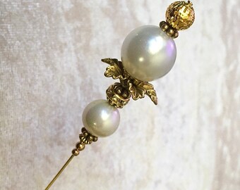 May include: A gold and white pearl hat pin with a decorative floral design.