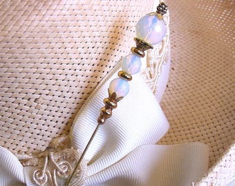 May include: A gold hat pin with iridescent white beads and a gold filigree design. The pin is on a straw hat with a white ribbon.