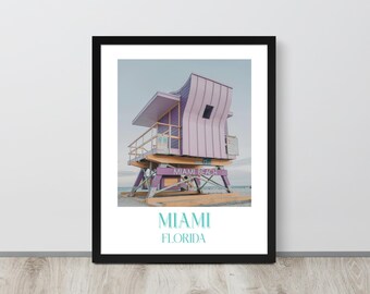 May include: A framed print of a pink and yellow lifeguard stand on a beach with the text "Miami Beach" and "Miami, Florida" below the image.