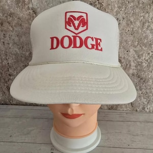May include: White trucker hat with a red Dodge logo and a ram's head emblem.