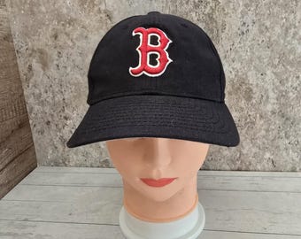 May include: A black baseball cap with a red "B" embroidered on the front. The cap has a curved brim and white stitching detail around the "B".