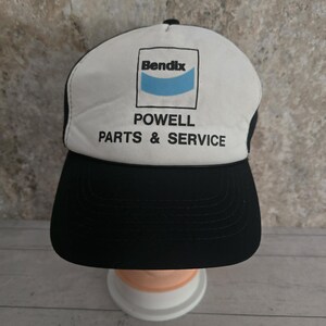 May include: A black and white trucker hat featuring the Bendix logo and the text "POWELL PARTS & SERVICE". The hat has a black peak and a white front panel with a mesh back.
