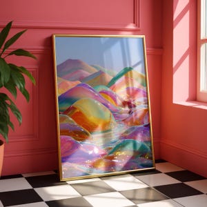 May include: A framed art print featuring a colorful, abstract landscape. The artwork depicts rolling hills in shades of yellow, orange, pink, and blue, with a glossy, reflective surface. The frame is gold, and the print is leaning against a pink wall.