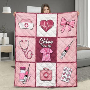 Puede incluir: Manta acolchada rosa y blanca con ilustraciones médicas. Los diseños incluyen un gorro de enfermera, un corazón con línea de pulso, un lazo, un estetoscopio, una jeringa, pastillas, un maletín médico y un uniforme de enfermera con "Chloe" y "Nurse Life".